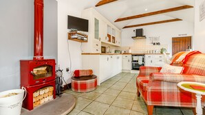 A cozy living room with a fireplace, a sofa, and a dining area with a kitchen in the background. - Willow Cottage (Driffield)
