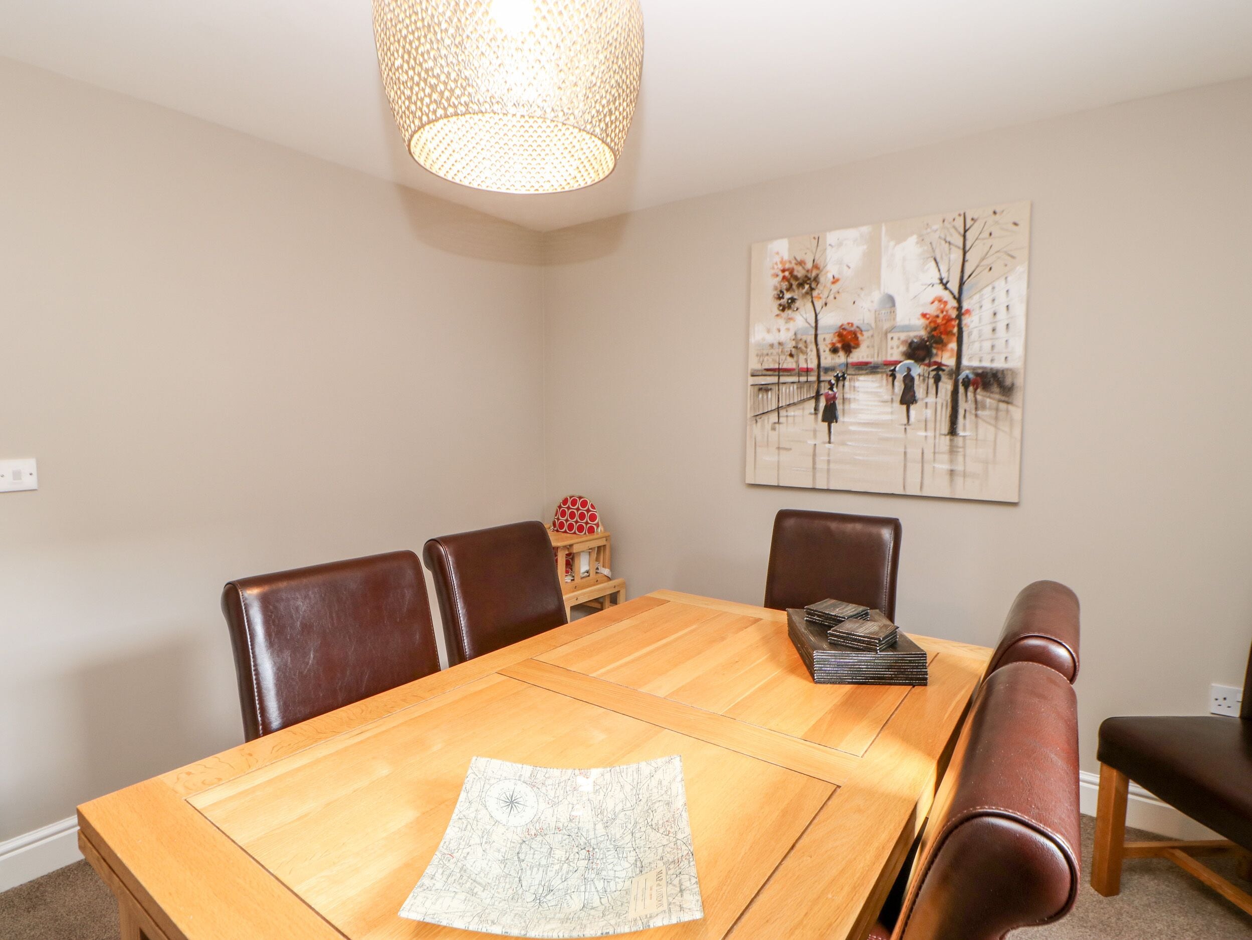 Een eetkamer met een houten tafel, lederen stoelen, een hanglamp en een schilderij aan de muur.