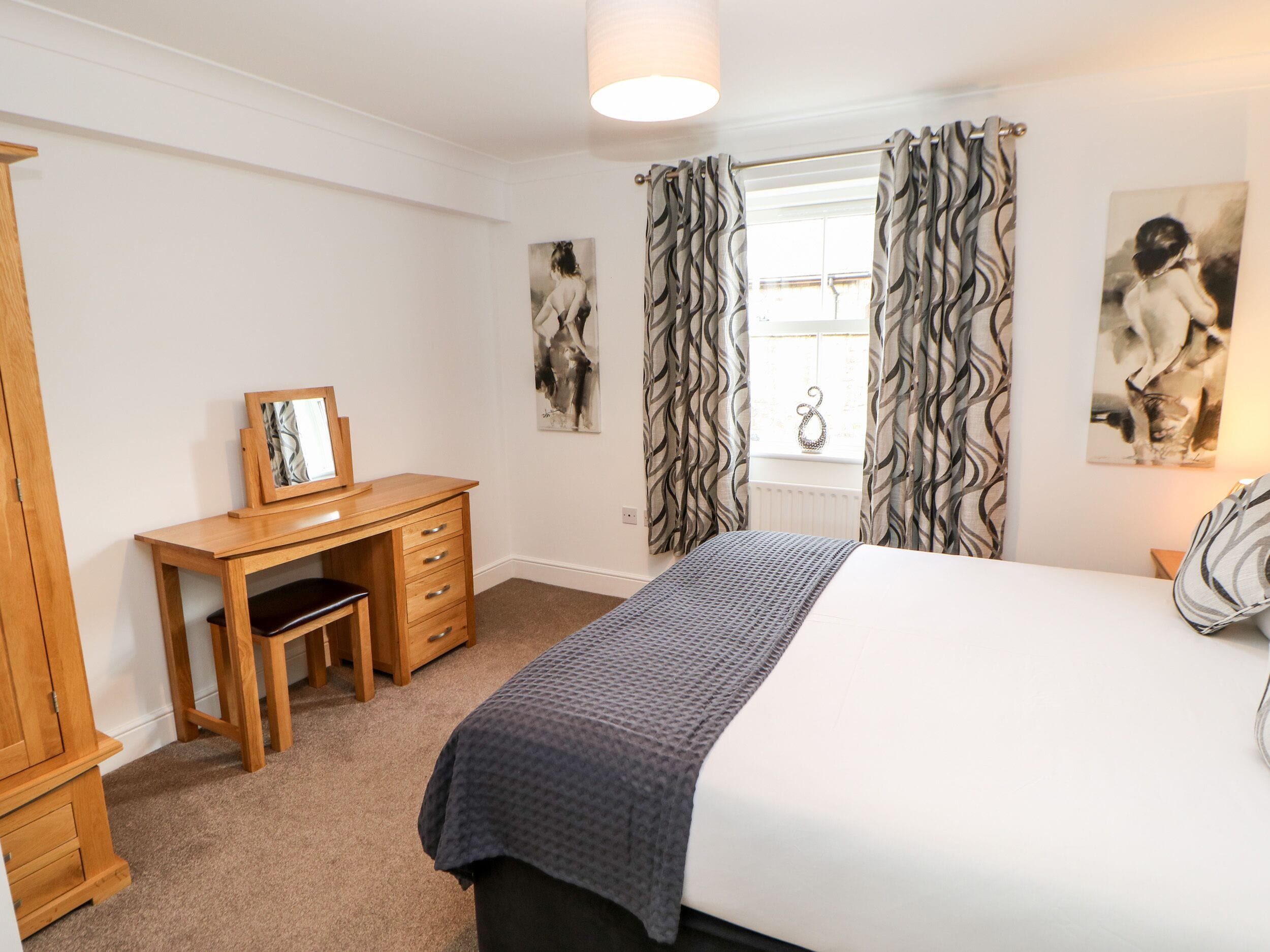 A bedroom with a bed, a desk, and two paintings on the wall.