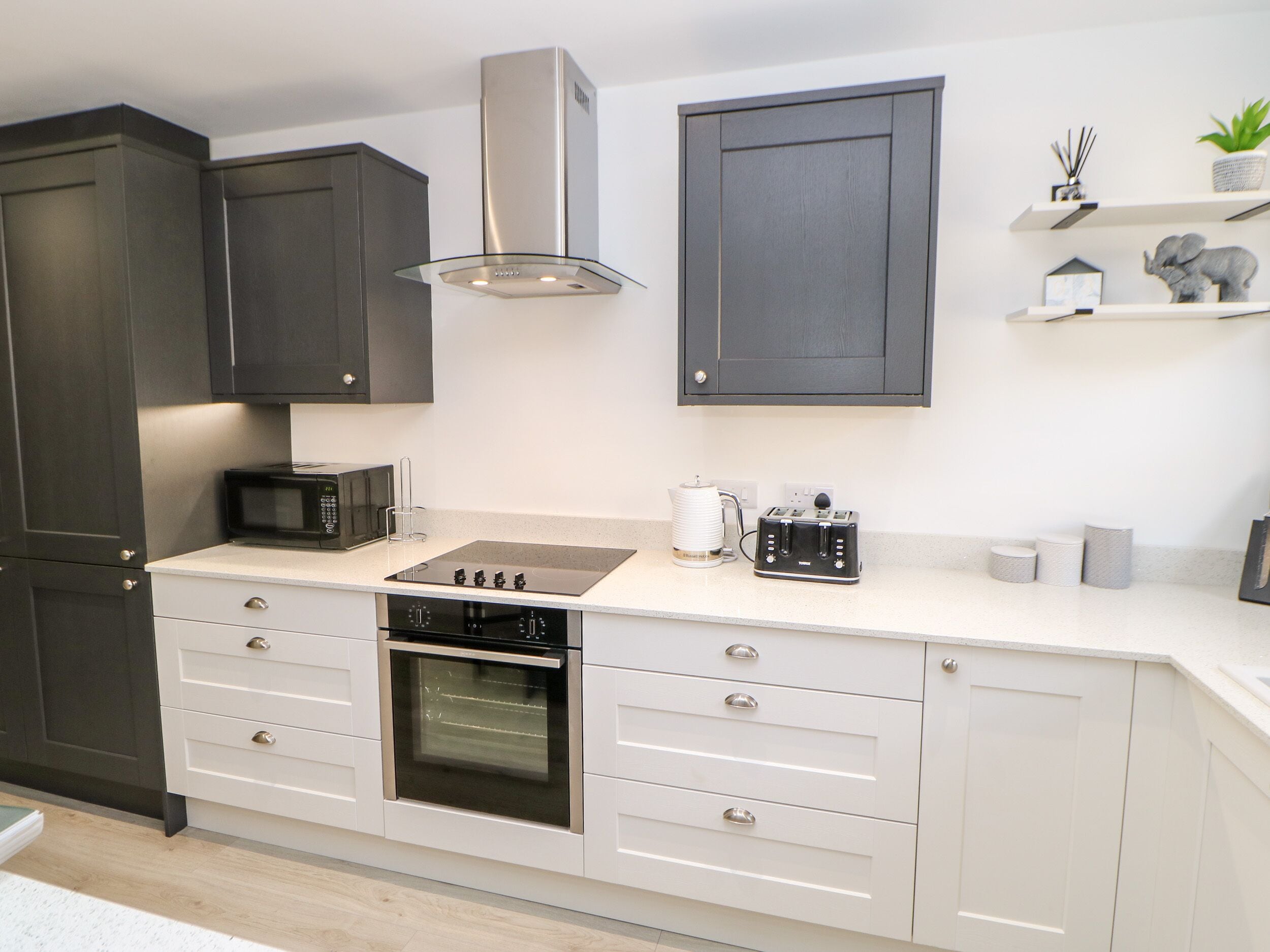 A modern kitchen with dark cabinets, a stainless steel range hood, a built-in oven, a microwave, and a toaster.