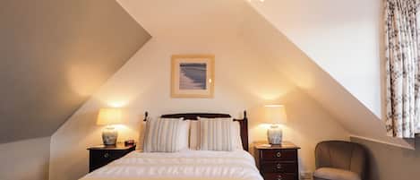 A bedroom with a bed, two bedside tables, a chair, a chandelier, and a picture on the wall.
