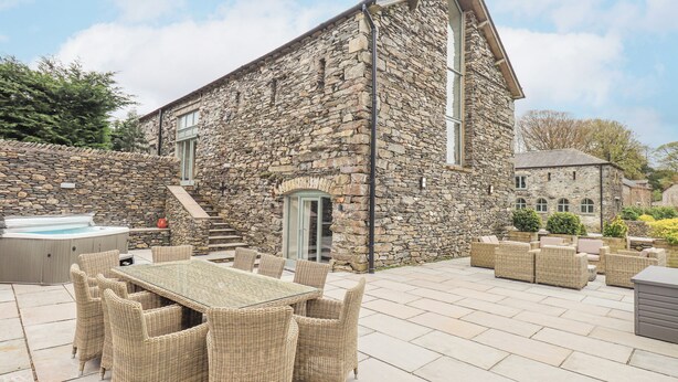 A stone building with a patio area featuring wicker furniture and a hot tub. - Oak Cottage (Ulverston)