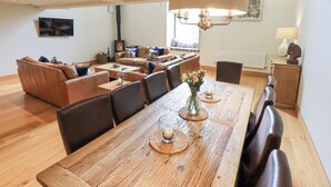 A spacious living area with a wooden dining table, leather sofas, and a fireplace. - Oak Cottage (Ulverston)