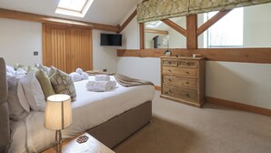 A bedroom with a bed, a wooden dresser, a TV, a window, and a ceiling light. - Oak Cottage (Ulverston)