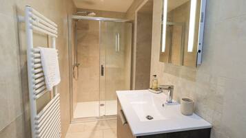 A modern bathroom with a glass shower enclosure, a white sink, and a large mirror.