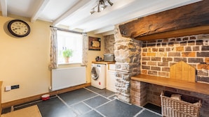 A laundry room with a stone wall, a washing machine, a radiator, and a wooden shelf with a '2016' sign.