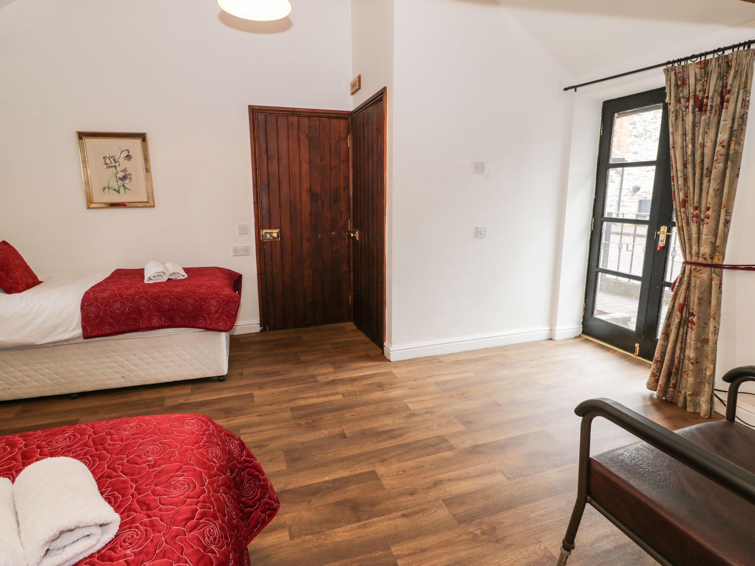 Une chambre avec deux lits, une porte en bois et une fenêtre avec des rideaux.