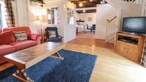 Ein Wohnzimmer mit einer Couch, einem blauen Sessel, einem Holztisch und einem Fernseher auf einem Holzboden.