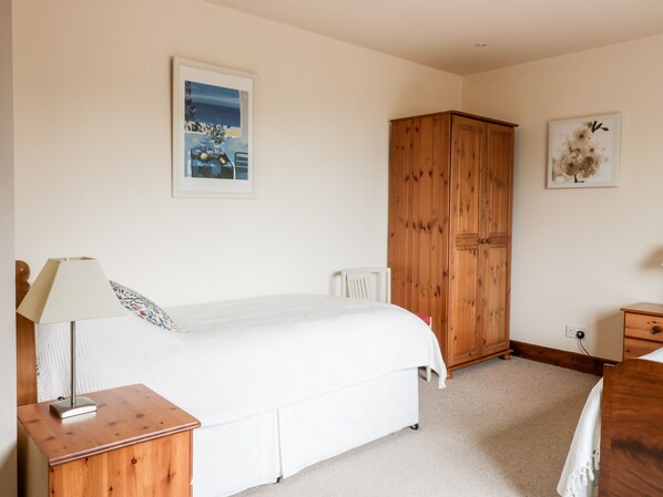 A bedroom with a bed, a wooden wardrobe, a bedside table with a lamp, and two framed pictures on the wall. - Courtyard Cottage (Duns)