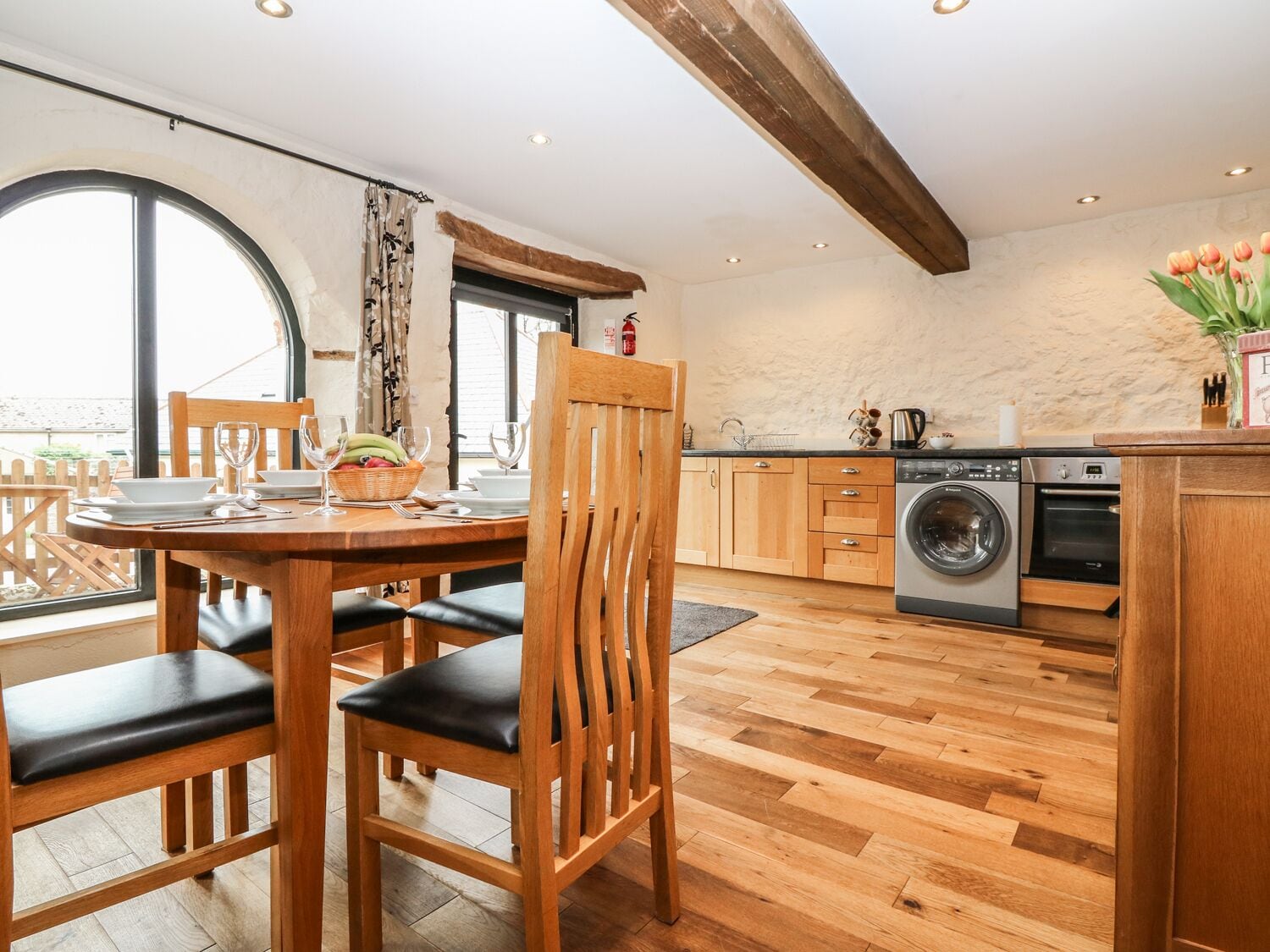 Een gezellige keuken met houten vloeren, een eethoek met een tafel gedekt voor twee personen, en een groot raam dat zorgt voor natuurlijk licht.