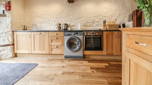 A kitchen with wooden cabinets, a washing machine, and an oven. - The Cider Barn (Newton Abbot)