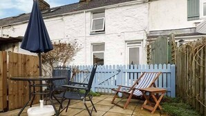 Une terrasse avec une table et des chaises, un parasol bleu et une clôture blanche.