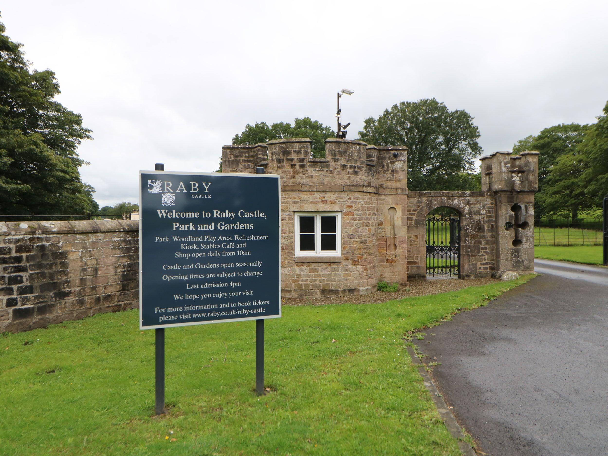 A sign for Raby's Castle, Park, and Gardens, indicating amenities like a park, woodland play area, refreshment kiosk, and stables café.