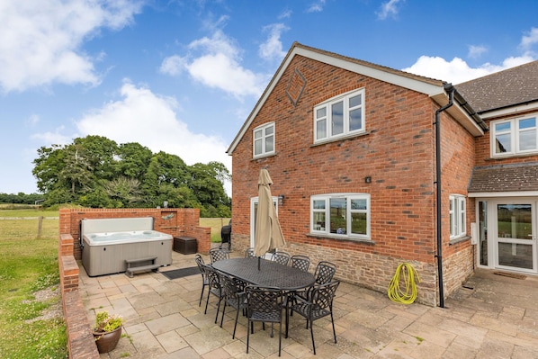 A brick house with a patio, a hot tub, and a table with chairs. - Wood Cottage (Tenbury Wells)