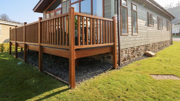 Una terraza de madera adosada a una casa con ventanas amplias y un cimiento de piedra.