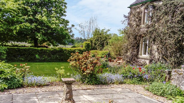 A garden with a stone fountain, lush greenery, and a building partially covered in ivy. - Church View (Buxton)