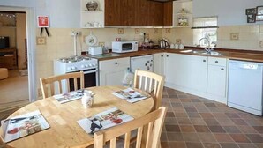 A compact kitchen with white cabinets, a wooden dining table, and a tiled floor. - Church View (Buxton)