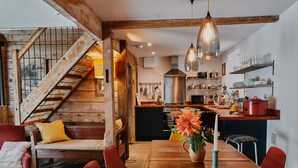 A rustic interior with a wooden staircase, a dining area with a wooden table and red chairs, and a kitchen with modern appliances. - The Hayloft (Ross-on-Wye)