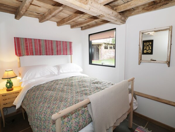 Une chambre à coucher avec un lit en bois, une fenêtre donnant sur un immeuble en briques, un miroir et une lampe sur une table de chevet.