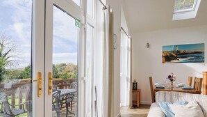 Une pièce dotée d’une porte-fenêtre coulissante donnant sur une terrasse extérieure avec une table et des chaises. On y trouve un lit avec une literie à rayures et un tableau représentant un phare accroché au mur.