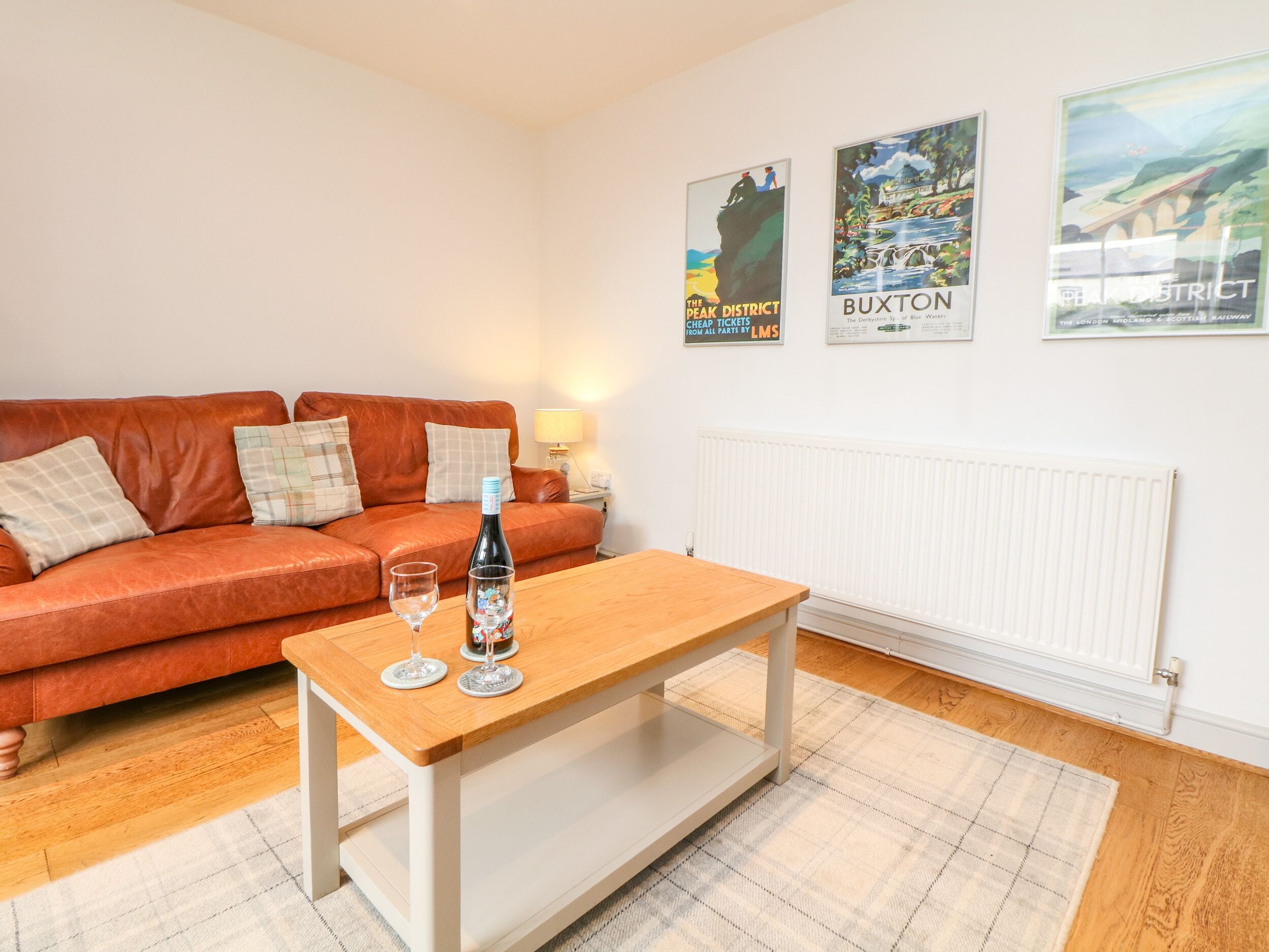 A living room with a red sofa, a wooden coffee table, two wine glasses, and a bottle. There are three posters on the wall.