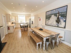 A spacious kitchen with wooden flooring, a central island, and a large painting of a lighthouse on the wall. - Hideaway House at The Hideaway (Tenby)