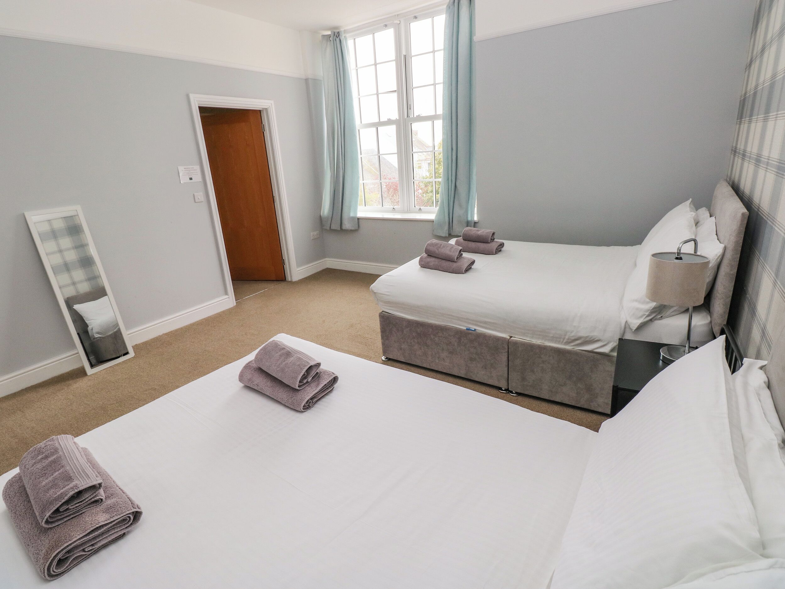 A hotel room with a large bed, a bedside table, a mirror, and a window with curtains.