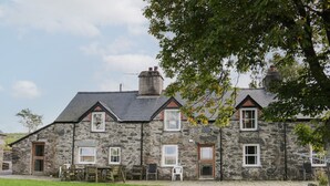 A stone house with a sloped roof, multiple windows, and a grassy yard. - Bryn Dedwydd Farmhouse (Betws-Y-Coed)