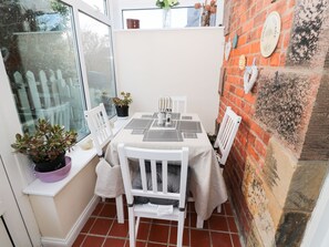 Enjoy meals in this charming dining area with a table for four, surrounded by a rustic brick wall and a view of a picket fence.