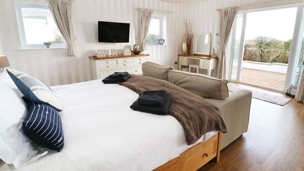 A bedroom with a bed, bedside tables, a TV, and a view of the outdoors.