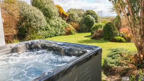 A hot tub in a garden with lush greenery and a clear sky.