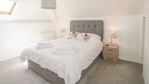 Un dormitorio con cama, mesitas de noche, un radiador y una ventana.