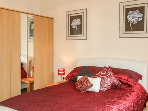 A bedroom with a bed, red bedding, a red lamp, and two framed floral pictures on the wall.