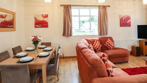 A living room with a dining table set for four, a sofa with patterned cushions, and artwork on the walls. - The Cabin (Ilfracombe)