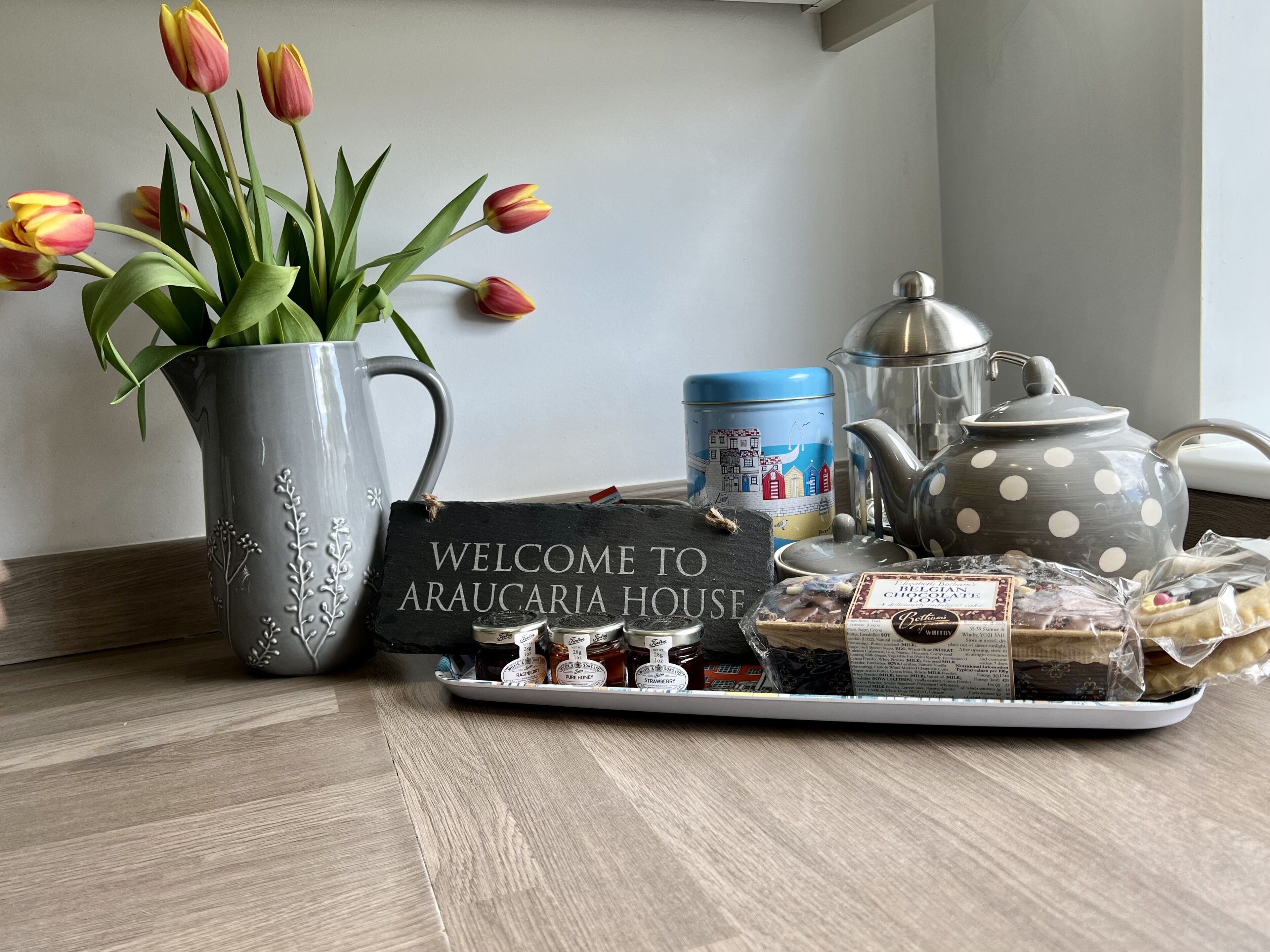 A tray with honey jars, a teapot, and a sign reading "Welcome to Araucaria House".