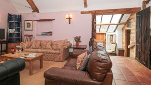 A cozy living room with a high ceiling, wooden beams, a floral sofa, a leather couch, and a bookshelf.