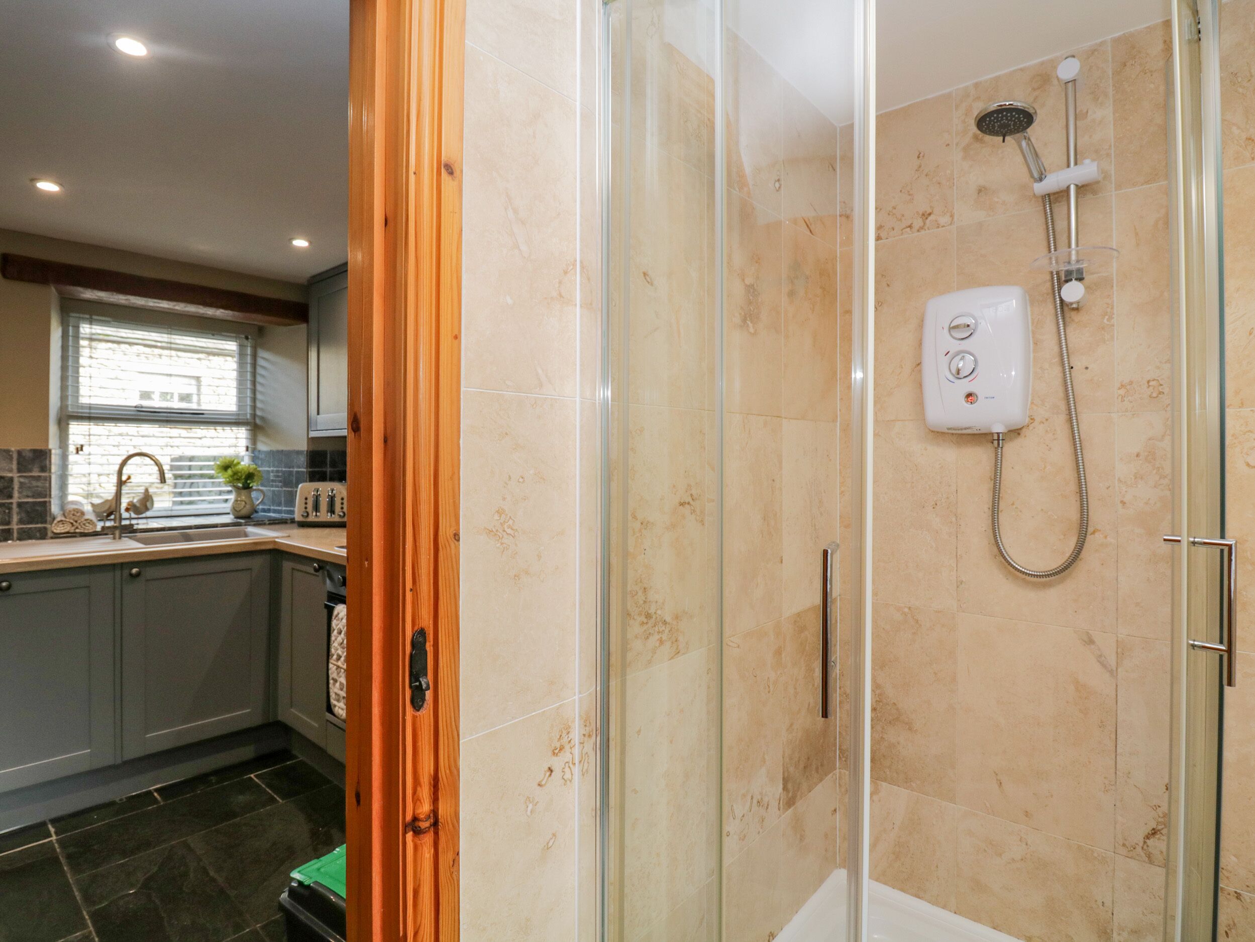 A modern bathroom with a glass-enclosed shower, a handheld showerhead, and a wall-mounted control panel.