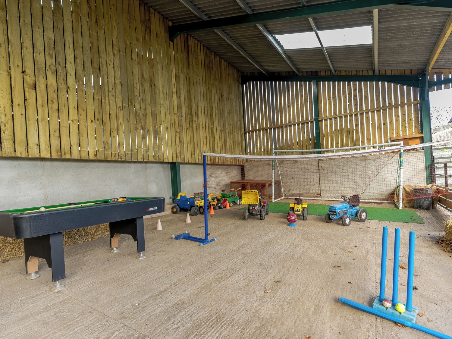 A covered indoor play area with a pool table, a small soccer goal, and various toys and vehicles.