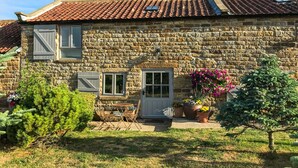 Une maison en pierre avec un toit en tuiles, un petit porche et des plantes en pot.