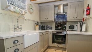 Une petite cuisine équipée d’un évier, d’une cuisinière, d’un four à micro-ondes et d’une horloge murale.