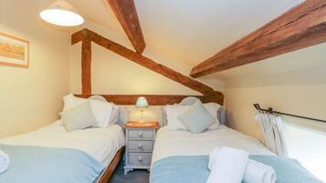 A bedroom with two beds, wooden beams, a nightstand, and a lamp.