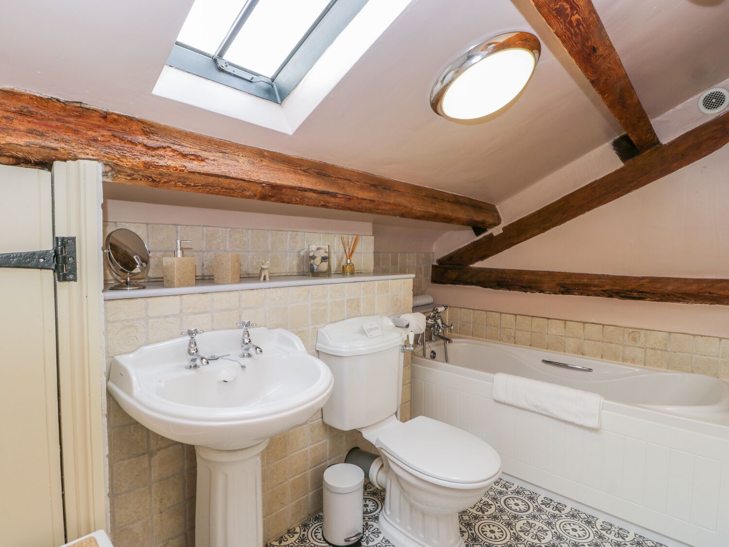 A bathroom with a skylight, a sink, toilet, bathtub, and a mirror on the wall.
