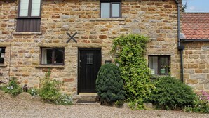 A stone building with a black door, two windows, and a small garden area. - Hayloft Cottage (Scarborough)