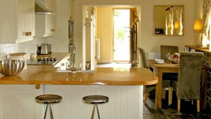 A kitchen with a wooden countertop, two stools, and a view of the dining area. - Valley View (Ross-on-Wye)