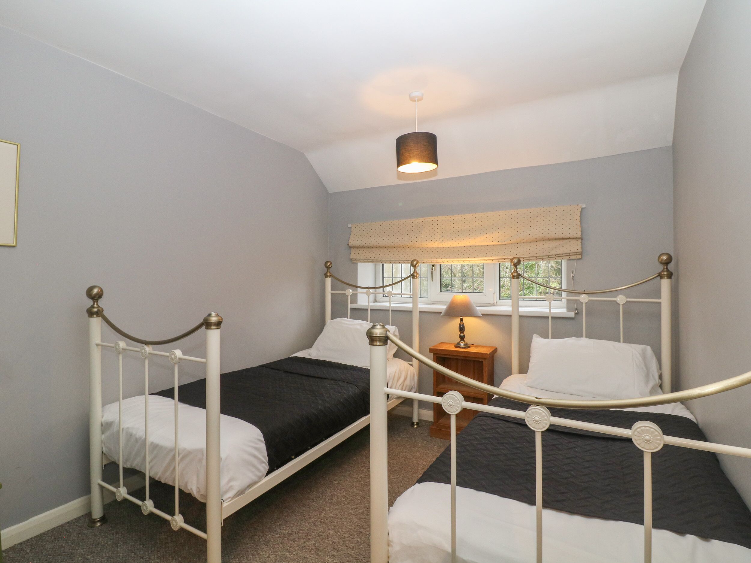 A room with two single beds, a small bedside table with a lamp, a window with a view, and a ceiling light.