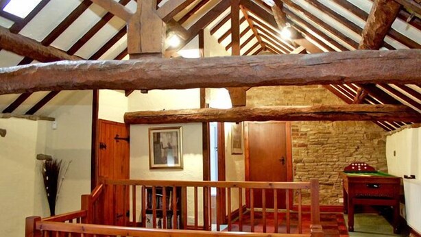 A rustic interior with exposed wooden beams, a stone wall, and a leather sofa. - The Loft (Chesterfield)