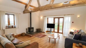 Amplia sala de estar con vigas de madera, chimenea, televisor y asientos cómodos.