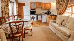 Ein gemütliches Wohnzimmer mit Sofa, Essbereich, Holzausbau und einer Küche mit Geräten.