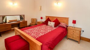 Ein Schlafzimmer mit einem Bettgestell aus Holz, einem großen Spiegel, einer Holzkommode und einer roten Polsterbank.