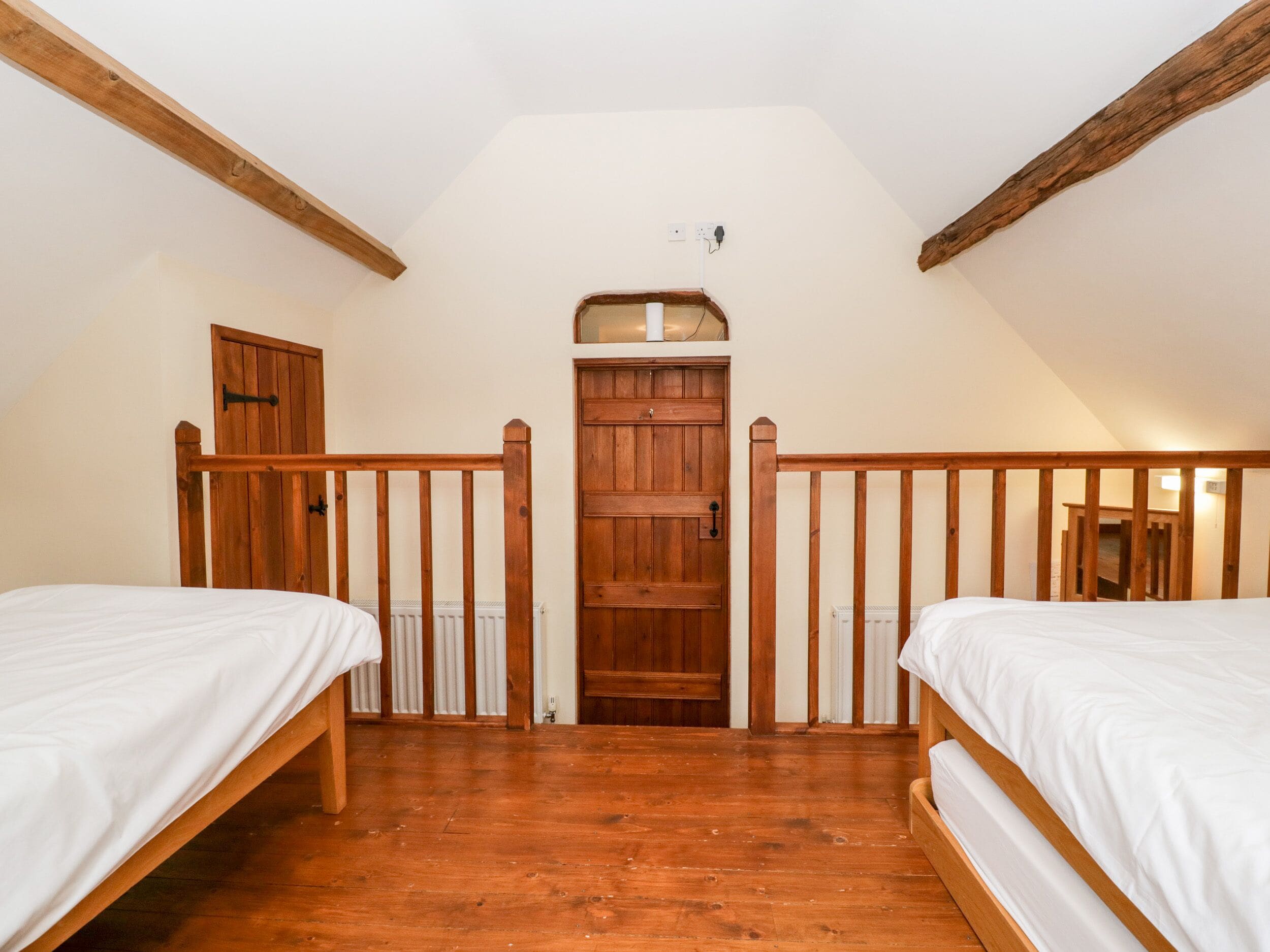 Un dormitorio con dos camas de madera, una puerta de madera y un techo blanco.